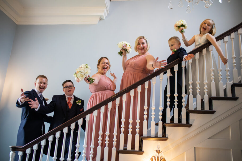 Bridesmaids and groomsmen standing on a staircase in a line smiling and waving their arms