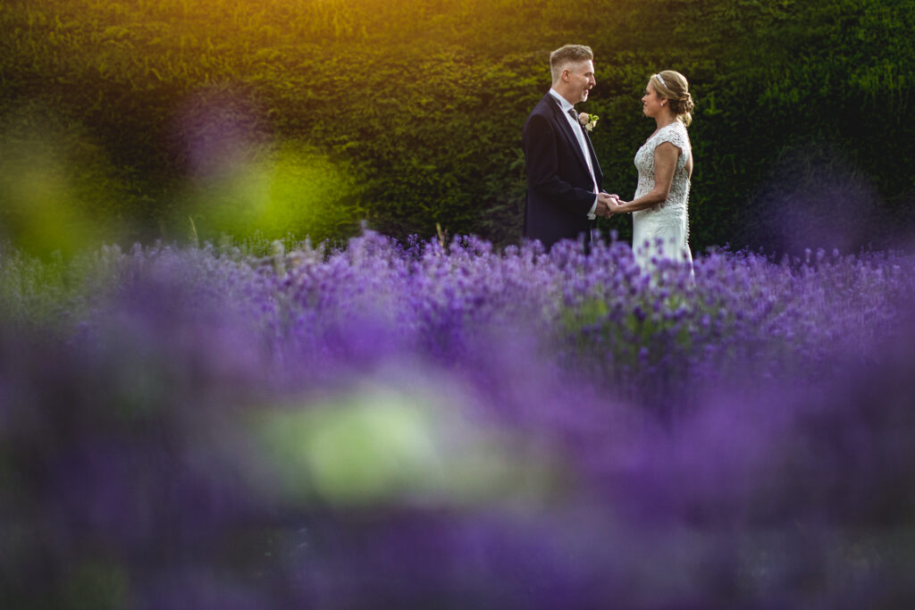 A bride and groom facing each other as they stand in a lavender field