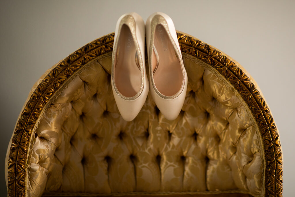 A pair of cream wedding shoes placed over an antique chair