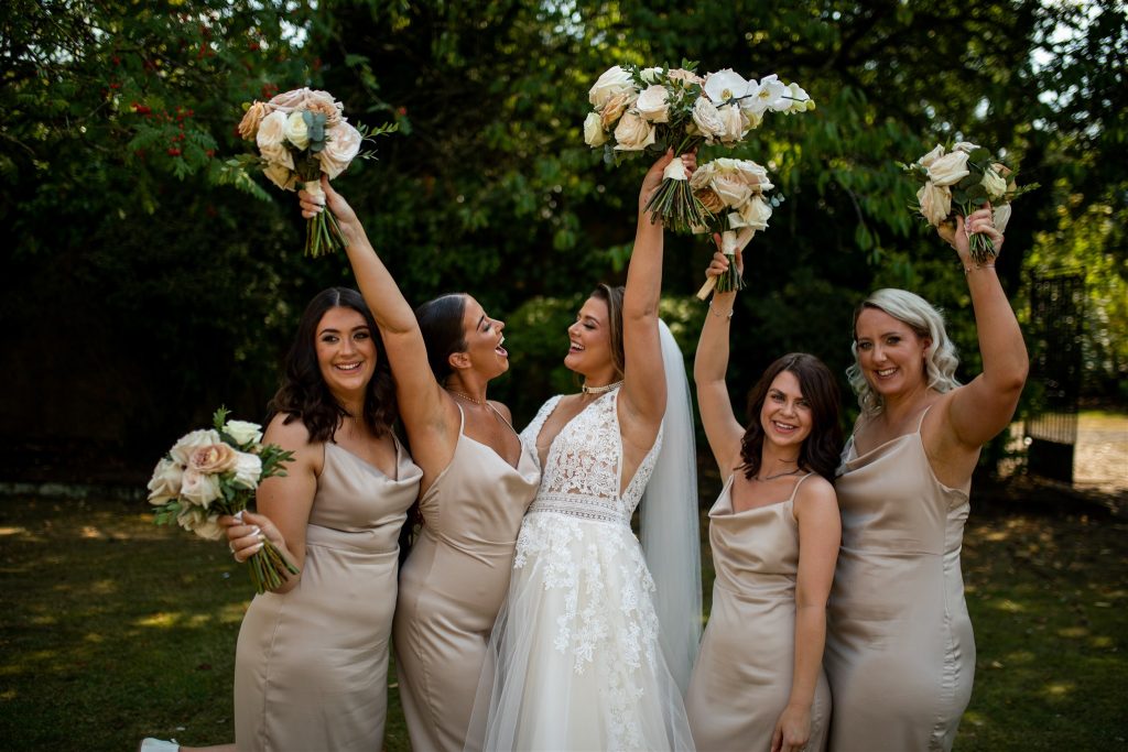 A bride and her bridesmaids holding up their flowers and smiling
