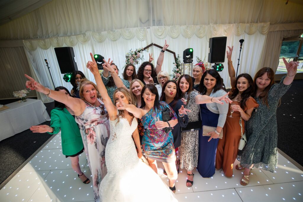 Bride and her bridesmaids smiling and dancing on the dance floor at Delta Hotels Forest of Arden.