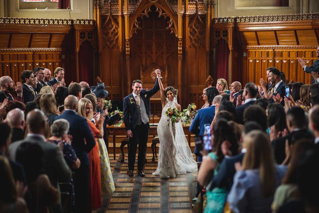 bride & groom cheering as they walk down the aisle after their wedding at Stanbrook Abbey with their guests clapping around them