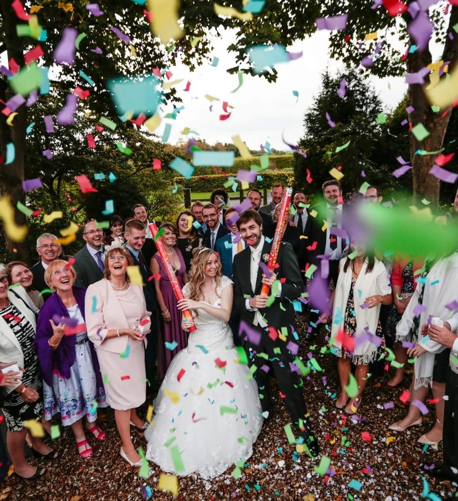 Confetti being thrown at a wedding with everyone surrounding the bride and groom