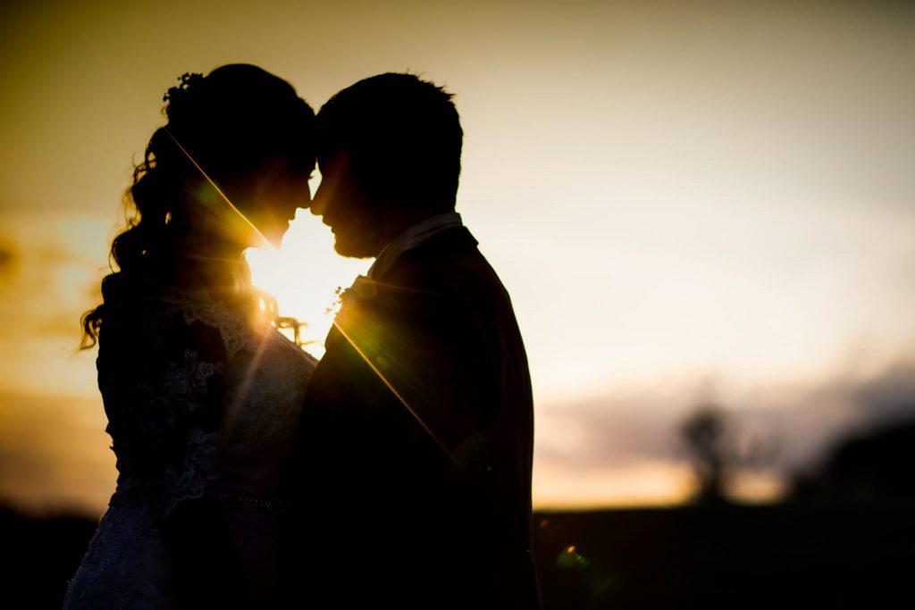 Bride and groom facing each other as the sun shines through them