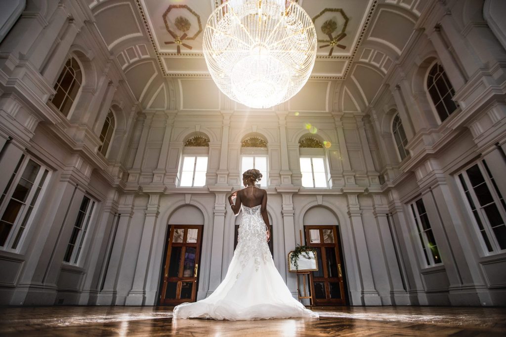 Bride standing under a large chandelier with sun appearing through a window