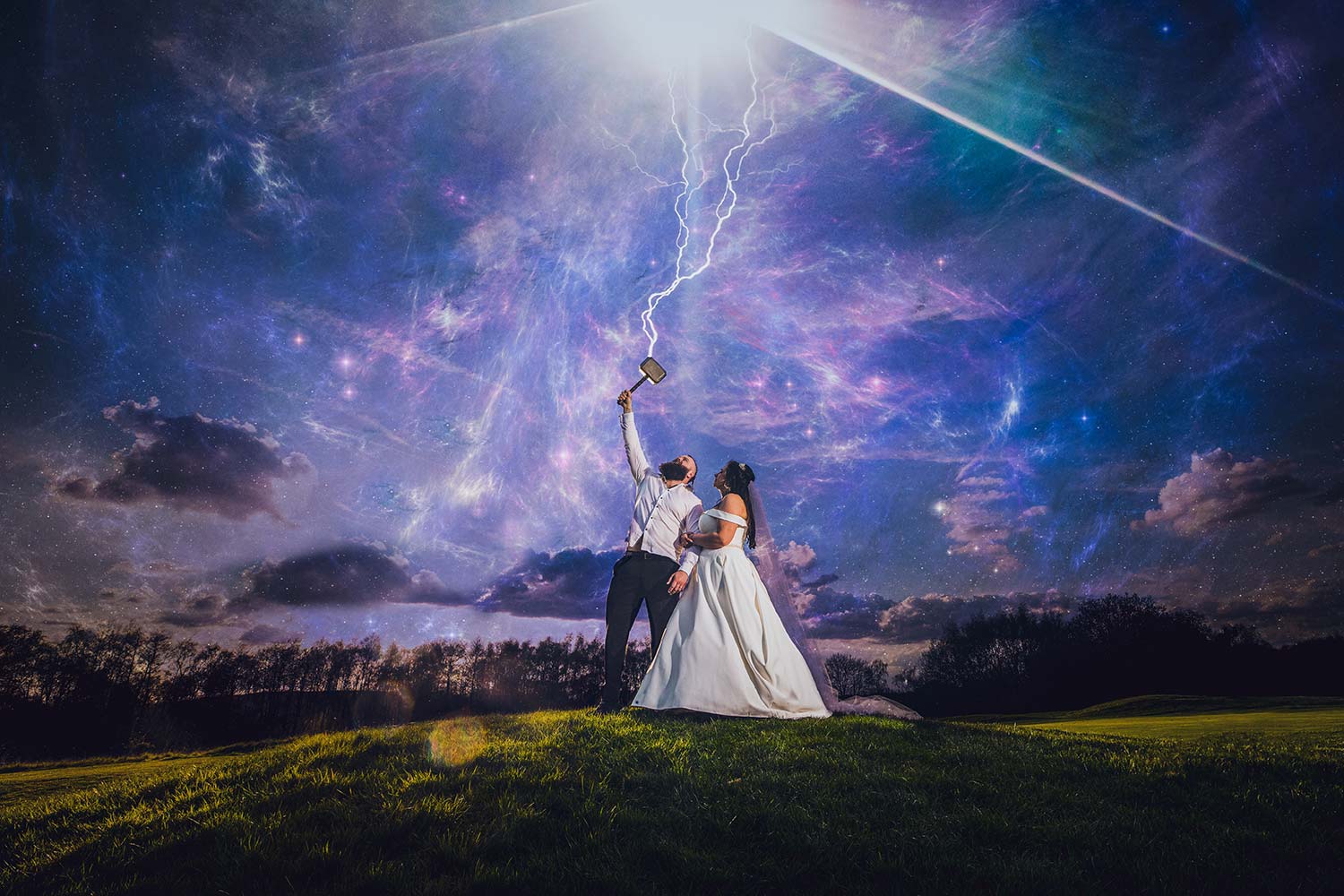 Married couple standing on a hill. The groom is holding a toy Thor hammer to the sky, and there is lightening coming out of it!