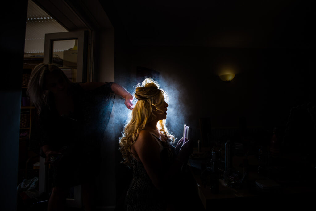 Bride having her hair sprayed and a light is placed behind her picking up the mist from the spray