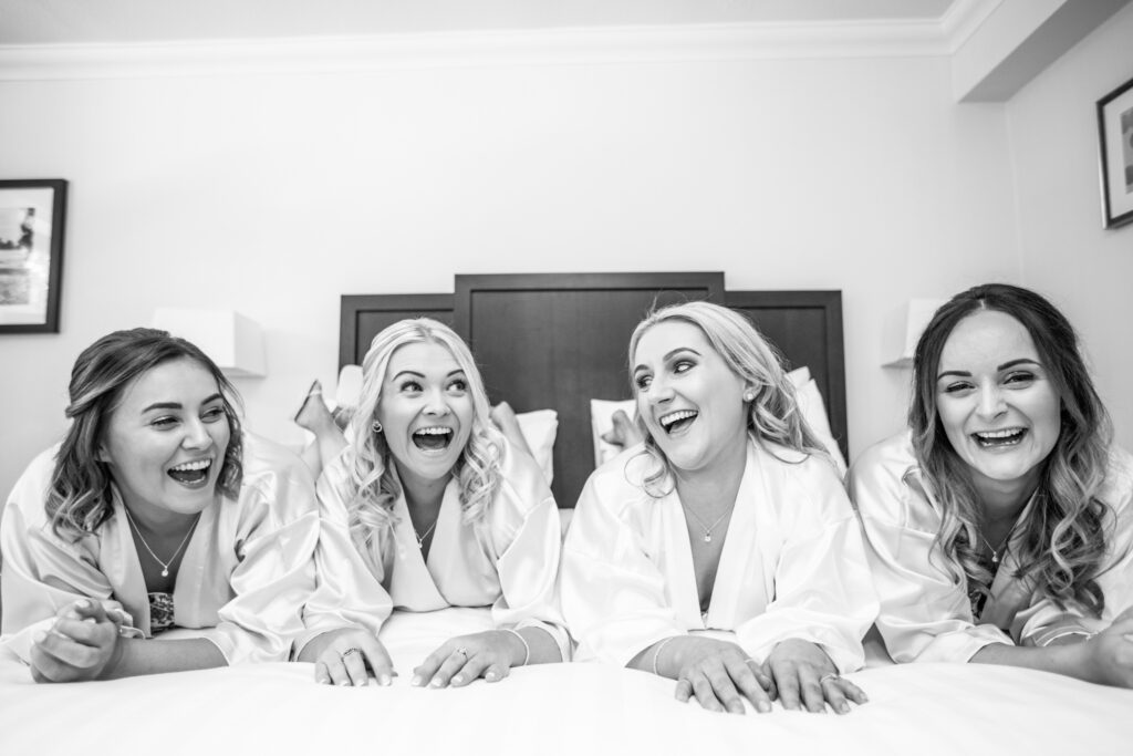 Bride lying on a bed with her bridesmaids laughing