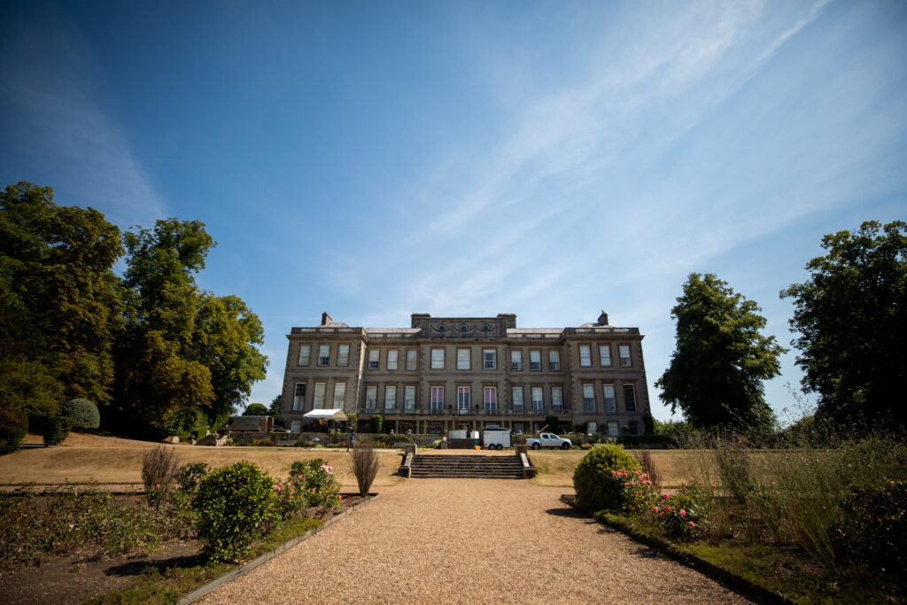 A large stately home set in the backdrop of the countryside. This image is shot looking up at the house from the bottom of the gardens