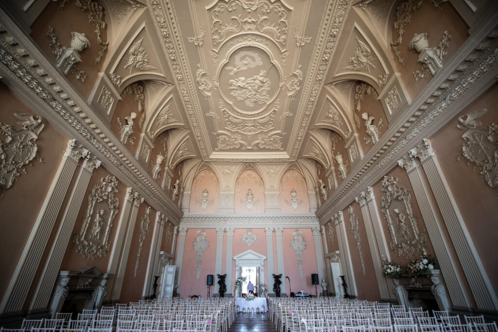 Hallway shot of a row of wedding chairs set on a marble floor including a large ceiling with art decorations