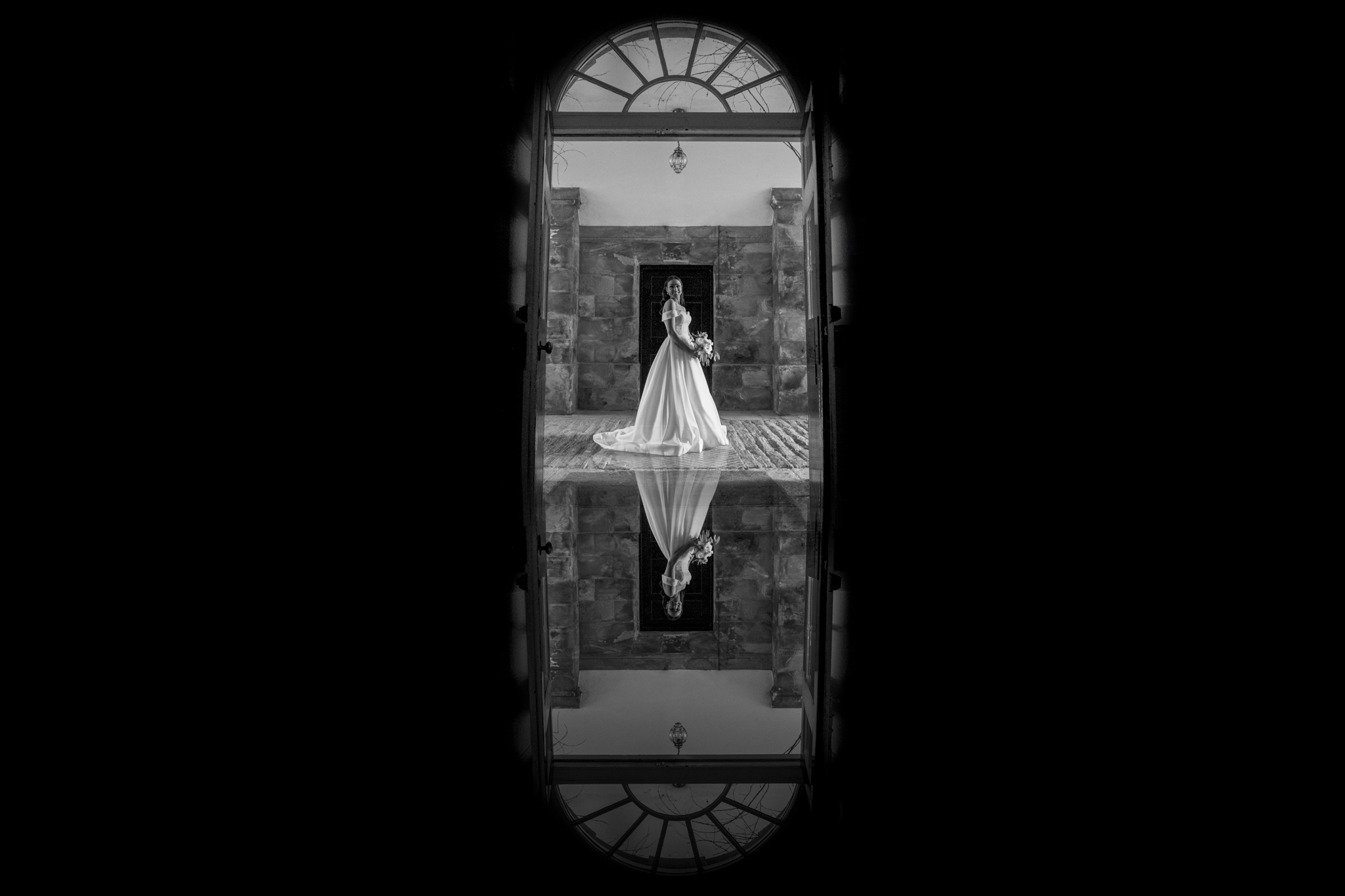 A black and white image of a bride looking forward. The shot is reflected by a mirror placed under the camera lens to create a reflection effect