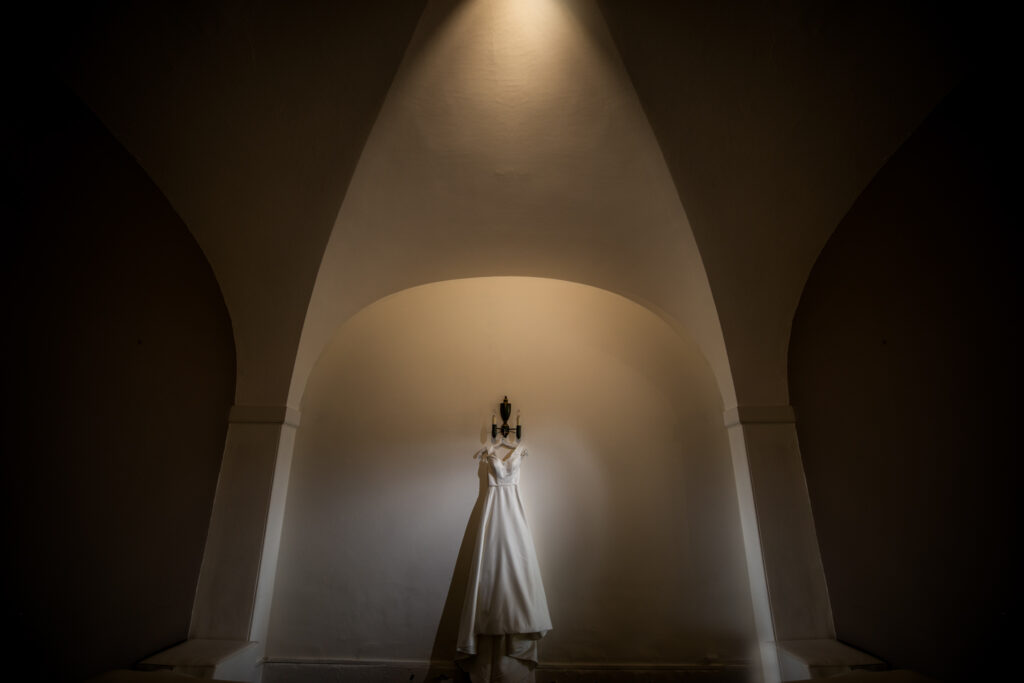 a wedding dress hung up on a white wall lit up with studio lighting creating a soft yellow effect on the wall