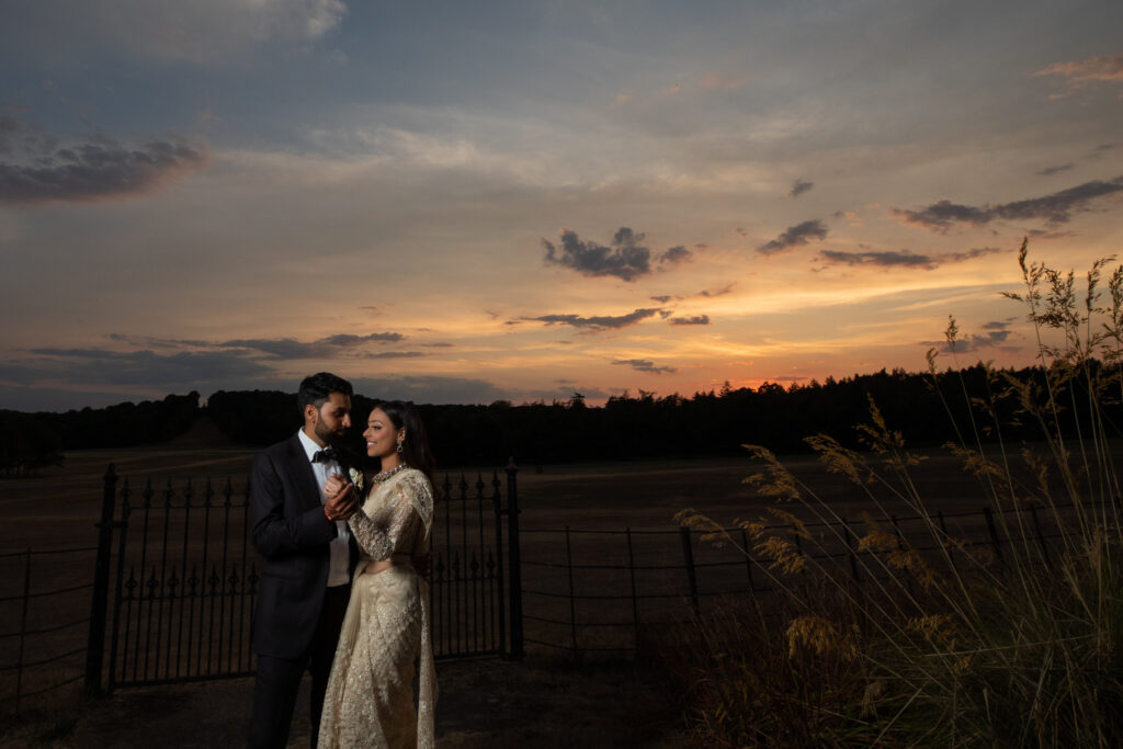 A bride and groom gholidng each other in the countryside with the sun setting in the background