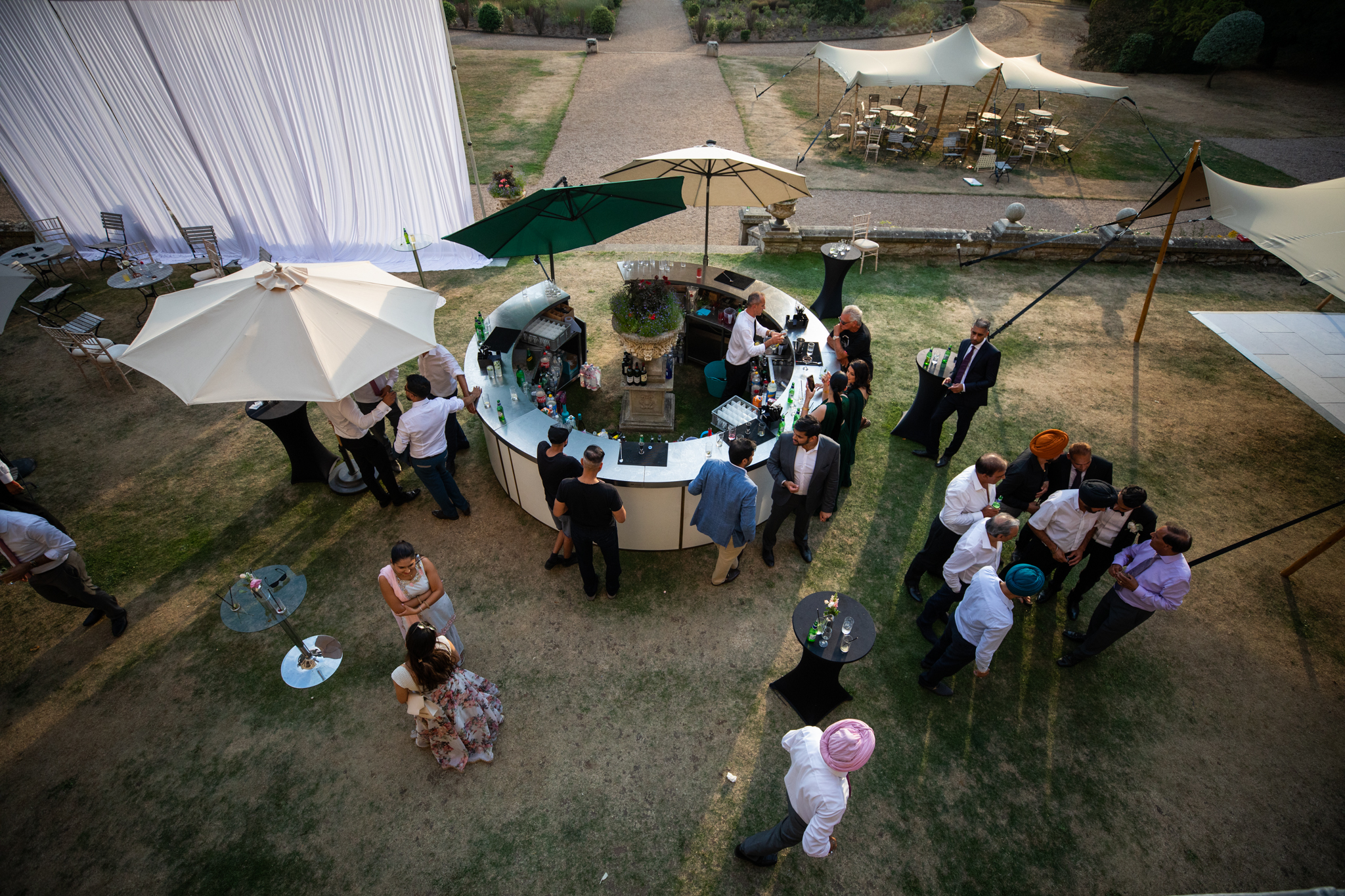 Ariel shot of guestrs at a wedding celebrating as they drink from the outside bar shaped in a circular design