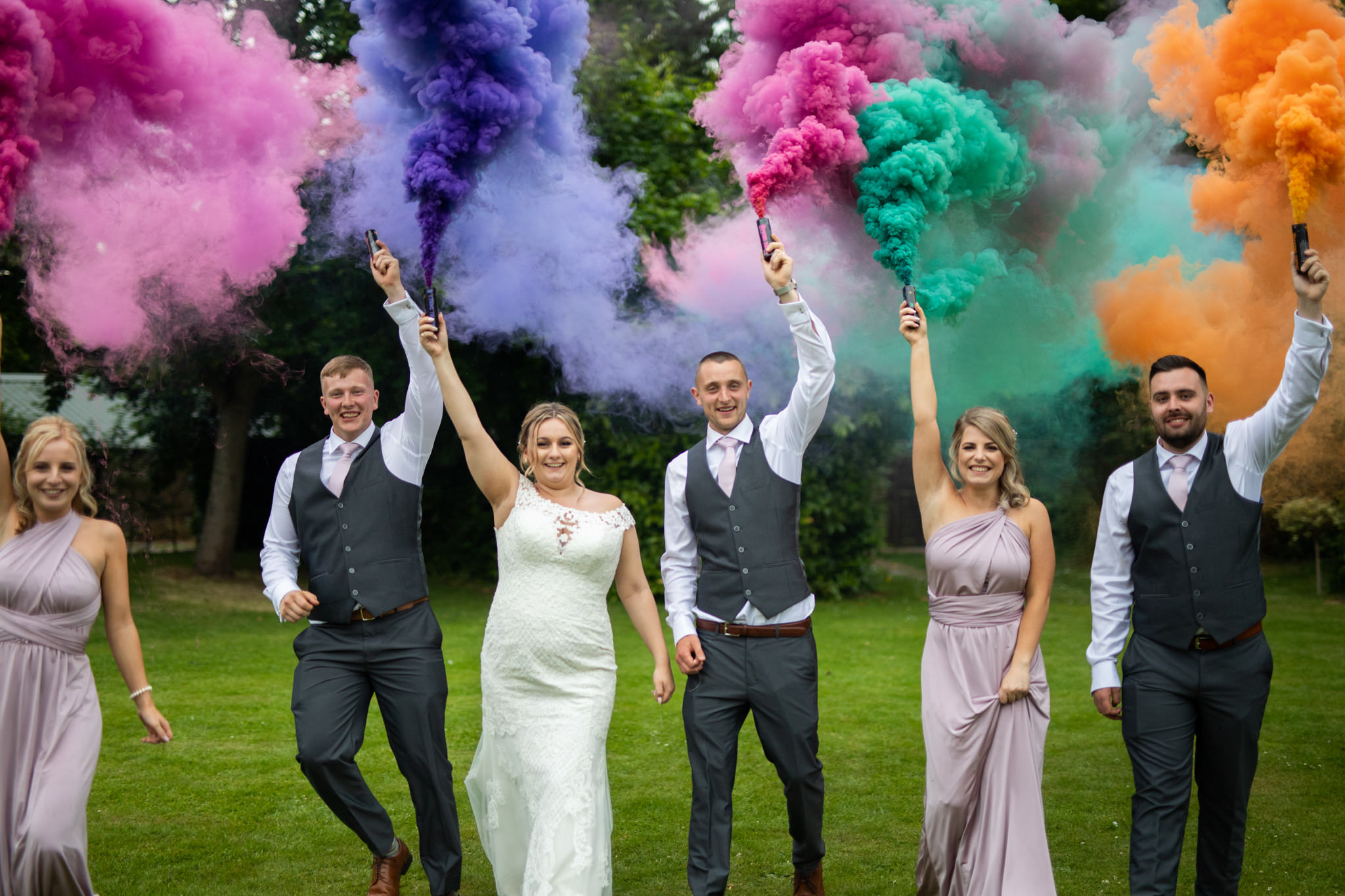 Bride and groom and their party walking with coloured smoke flares