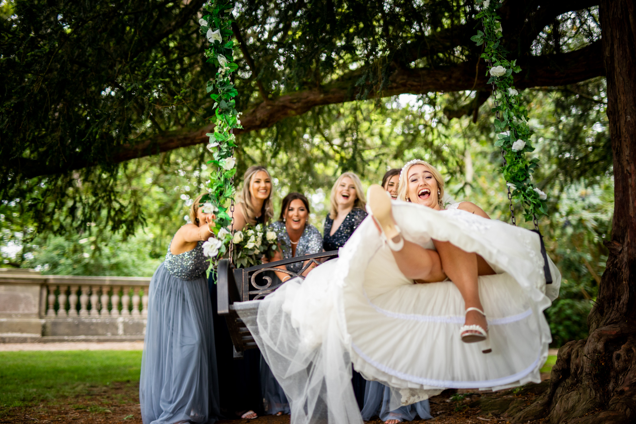 Bride laughing as she is pushed on a large swing by her bridesmaids