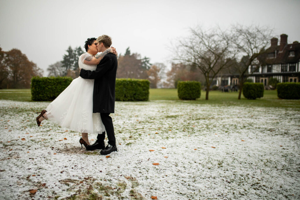 Bride and groom kissing as they embraces standing on some grass in the snow
