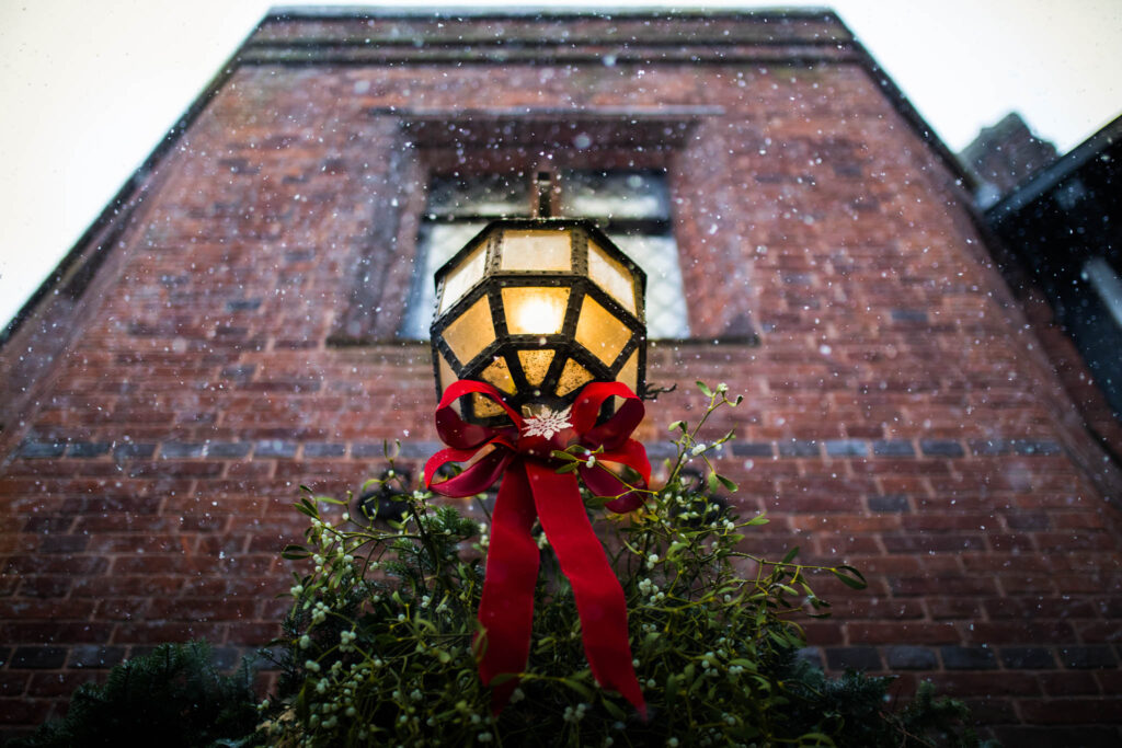Snowing photograph taken outside with a lantern with a red bow tied around it.